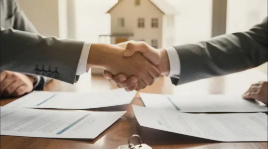 Poignée de main entre vendeur et acheteur avec clés et documents contractuels sur table en bois